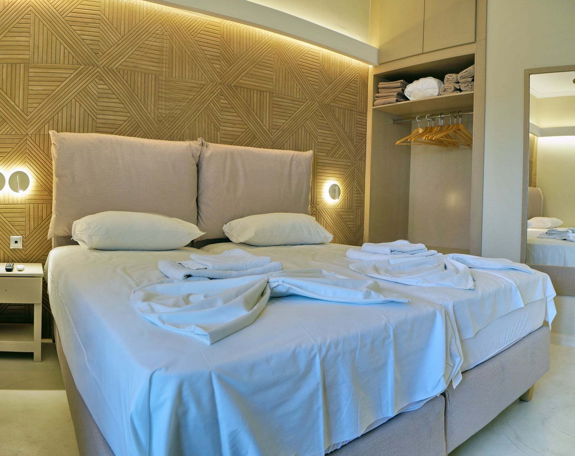 Una habitación de hotel moderna con una cama grande, dos mesitas de noche, un armario empotrado y un espejo.