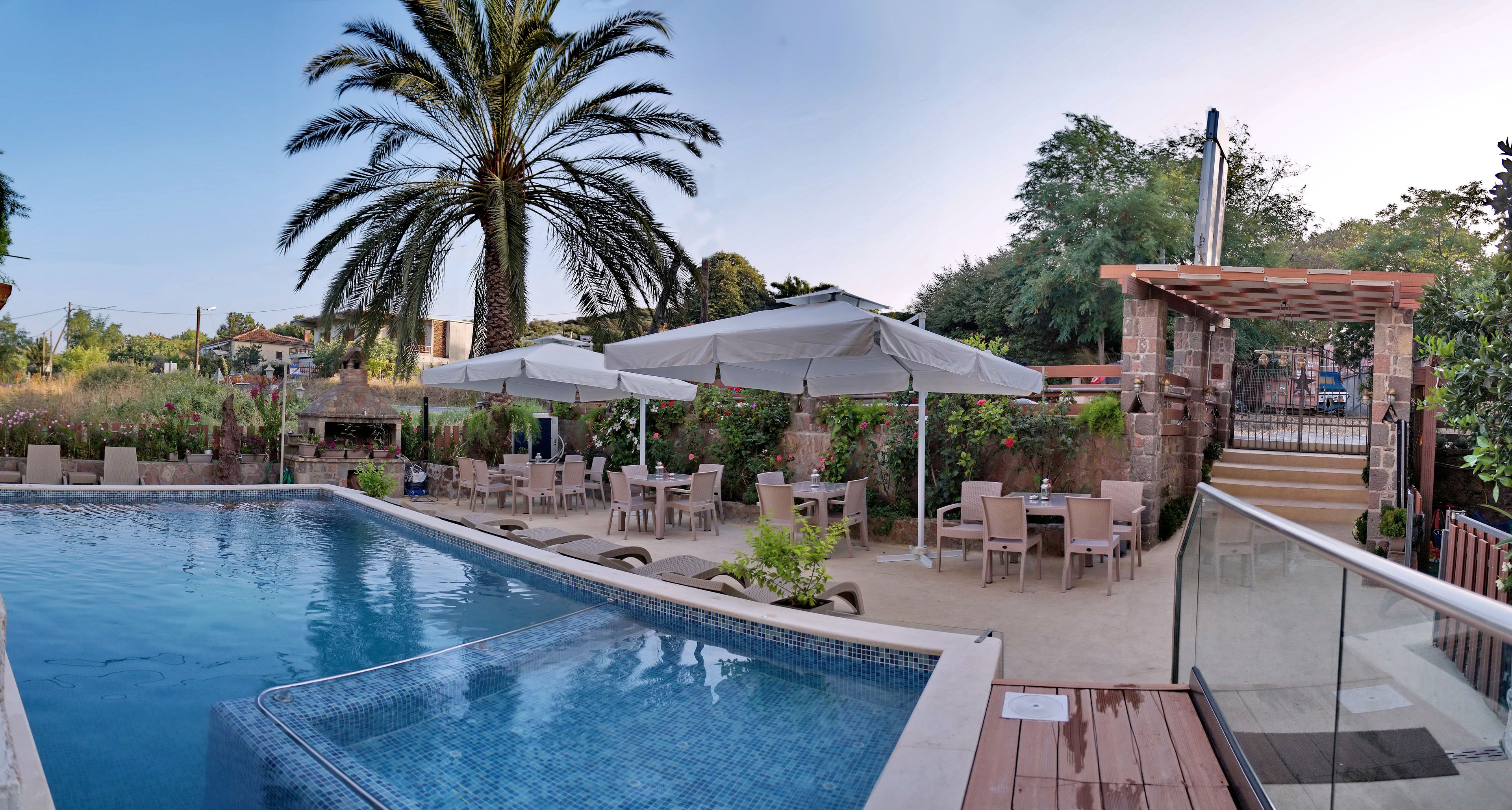 Piscina con sillones de descanso y sombrillas, rodeada de vegetación y una estructura de piedra.