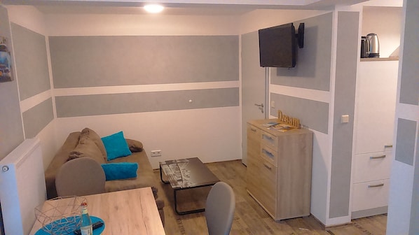 Une petite pièce, de taille modeste, comprenant un canapé, une table en bois, un téléviseur fixé au mur et un meuble avec des tiroirs.