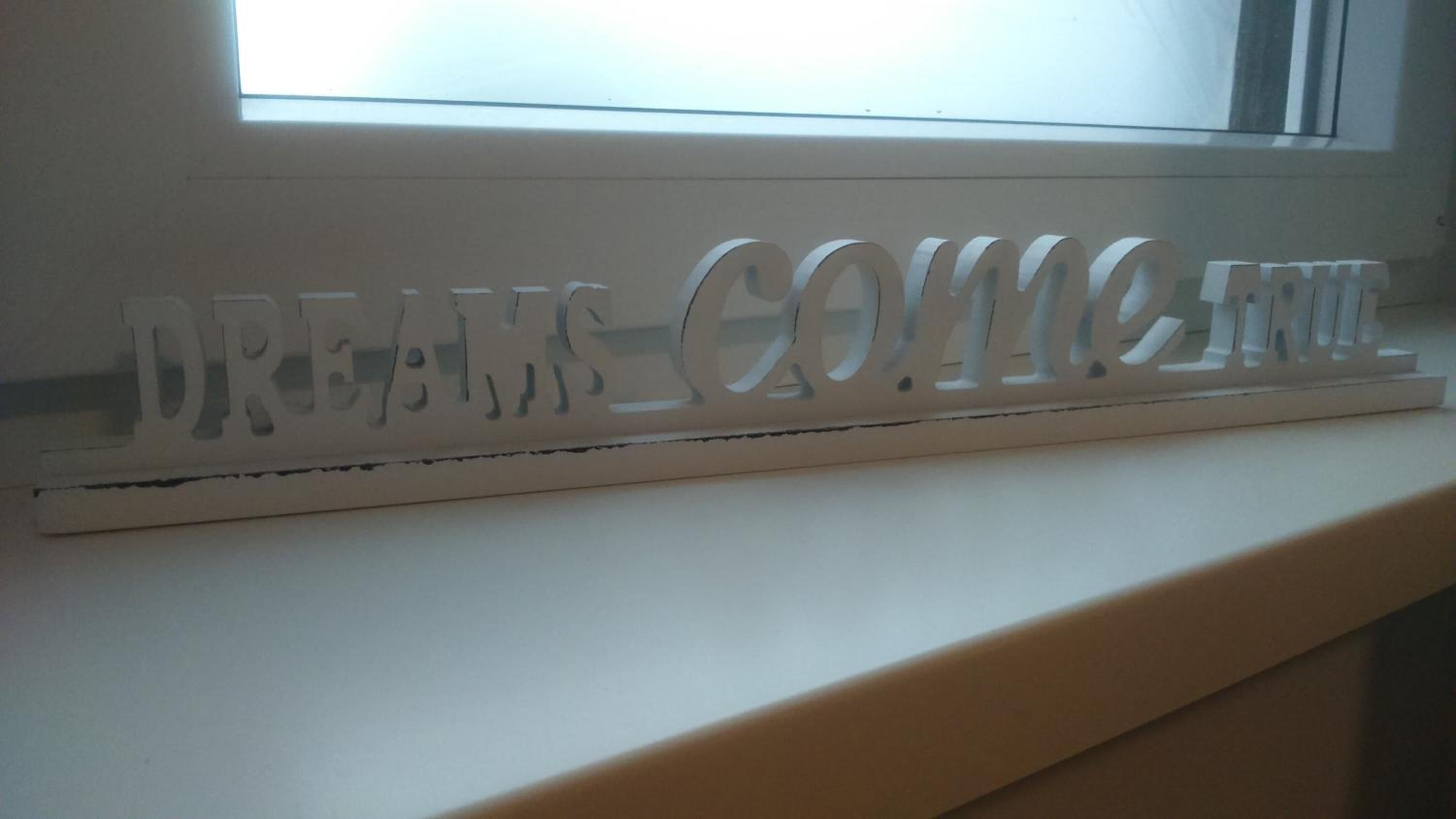 A white decorative sign with the words "DREAMS COME TRUE" on a window sill.