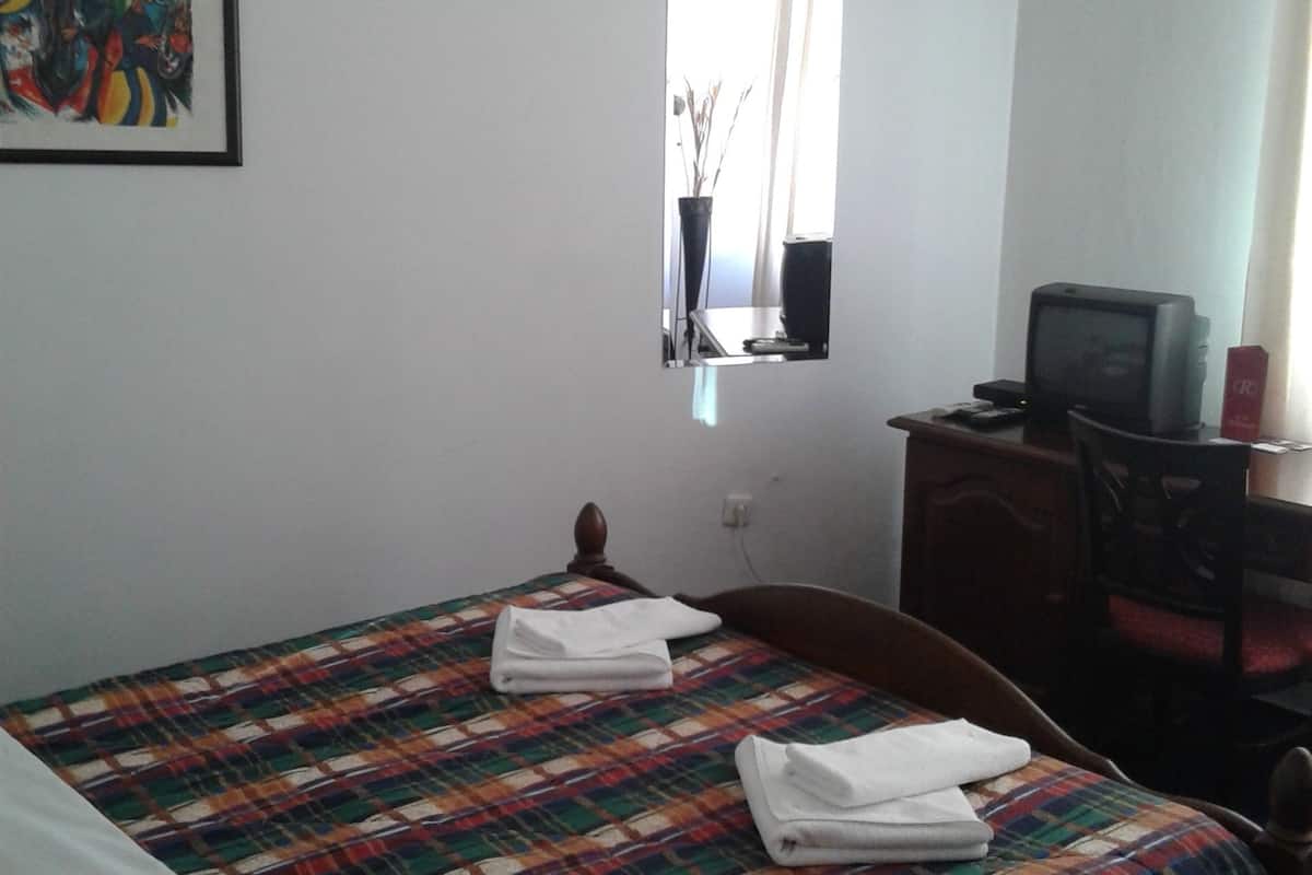 Habitación de hotel con una cama, un escritorio con computadora, aire acondicionado, una ventana con vistas y un cuadro en la pared.