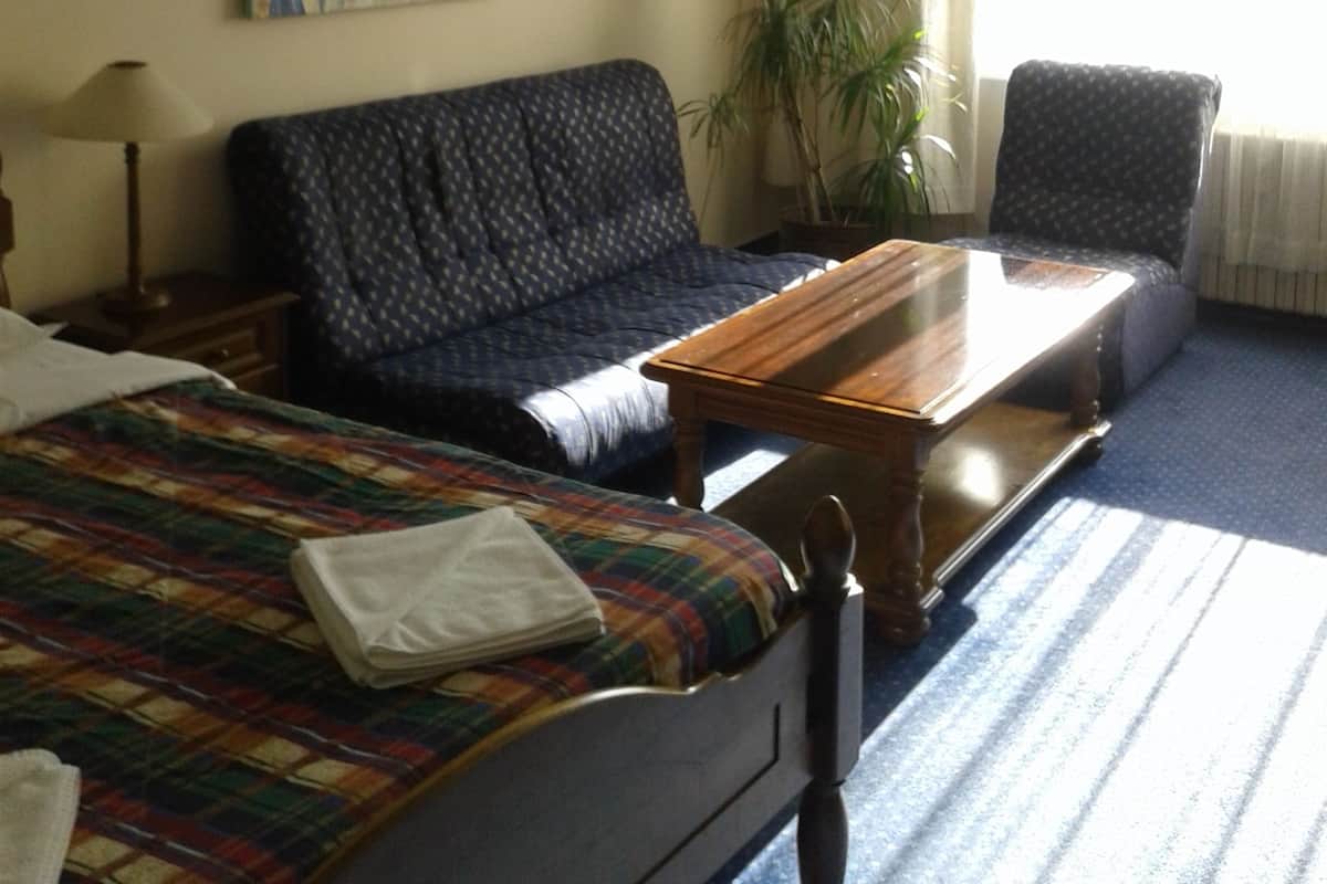 Habitación de hotel con cama, sofá, sillón, mesa, un cuadro en la pared y planta en maceta.