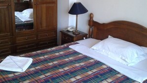 A neatly made bed with a plaid bedspread, a wooden wardrobe, a bedside lamp, and a painting on the wall. - Rotasar Hotel (Sofia)
