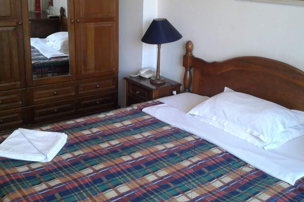 Una cama bien hecha con colcha escocesa, un armario de madera, una lámpara de noche y un cuadro en la pared.