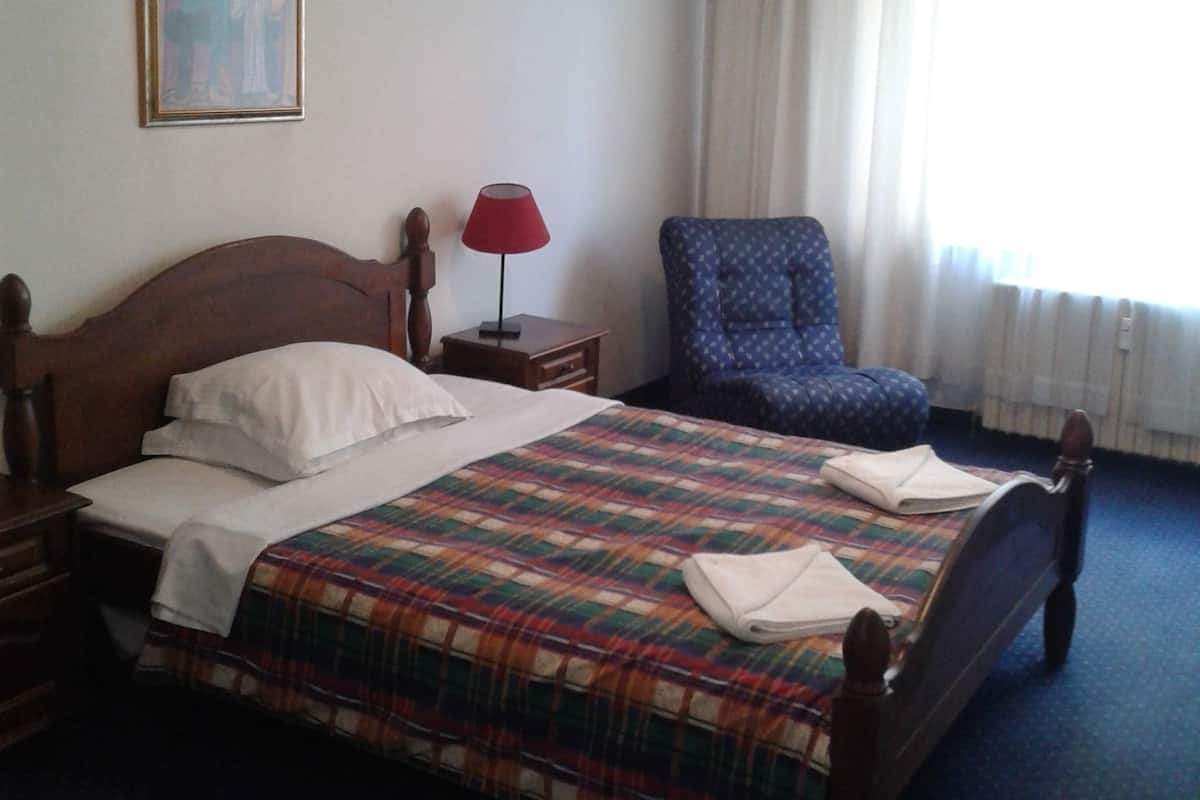 Una habitación de hotel con una cama, una silla, un cuadro en la pared y un equipo de aire acondicionado.