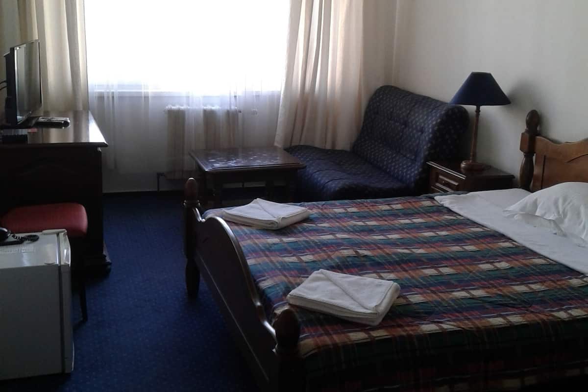 Una habitación de hotel con cama, una silla, escritorio, televisión y ventana con cortinas.