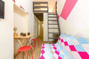 Habitación compacta con una cama litera, un escritorio de madera con taburetes, y una escalera que lleva a un altillo.