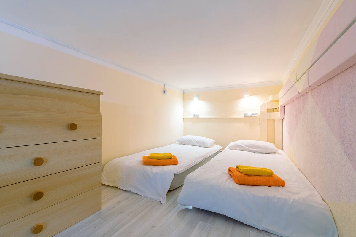 A room with two single beds, a wooden dresser, and a light-colored wall.