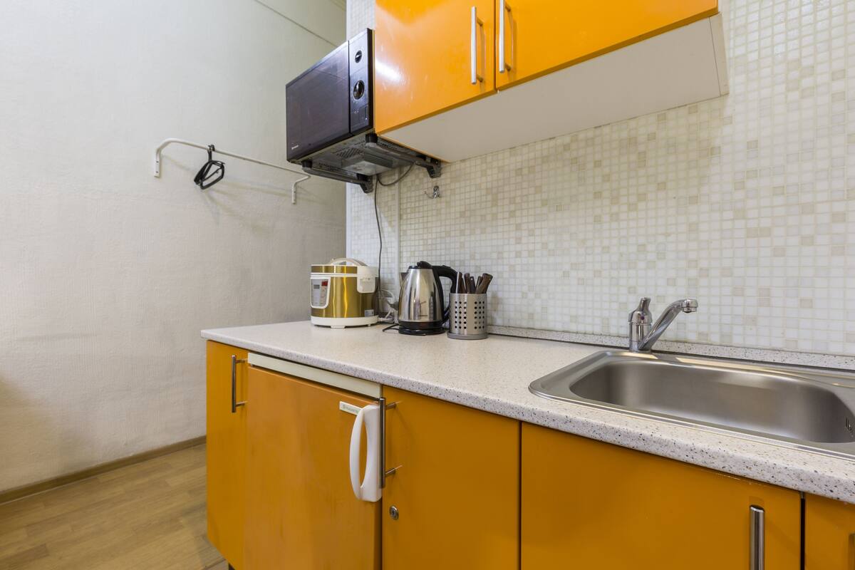 A kitchen with yellow cabinets, a stainless steel sink, and a microwave.