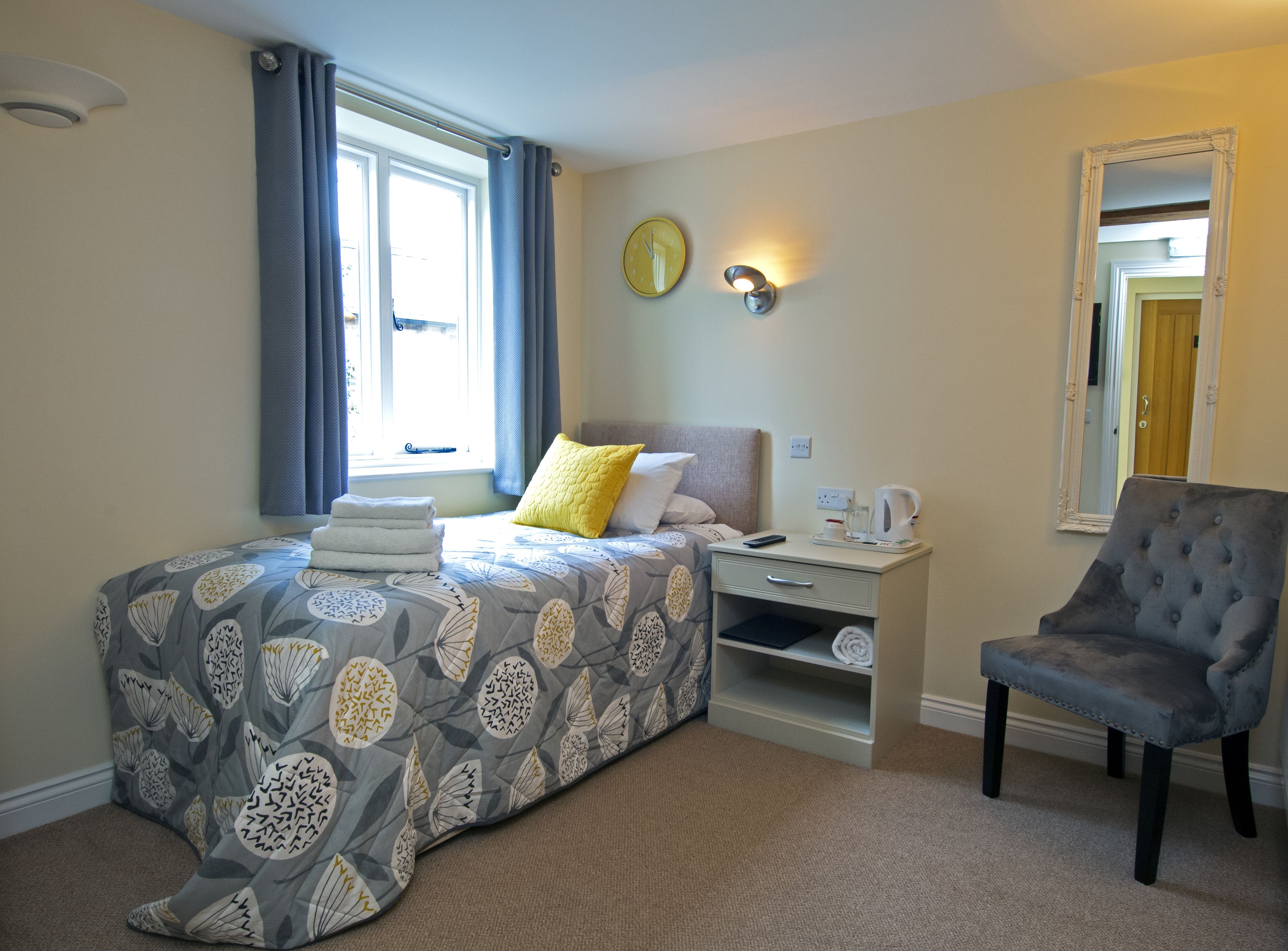 A hotel room with a bed, a chair, a nightstand, a mirror, and a window with curtains.