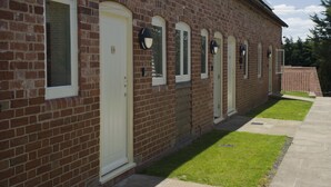 A brick building with multiple doors and windows, a paved walkway, and a small lawn area. - Alexander Park Resort (Ledbury)