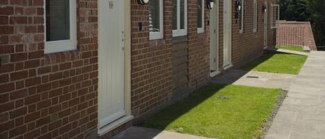 A brick building with multiple doors and windows, a paved walkway, and a small lawn area.