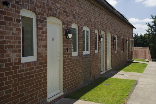 A brick building with multiple doors and windows, a paved walkway, and a small lawn area. - Alexander Park Resort (Ledbury)