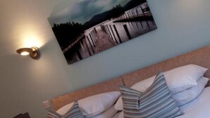 A hotel room with a bed, pillows, a painting, and a stack of towels. - Alexander Park Resort (Ledbury)