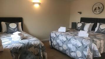 A hotel room with two beds, each with a headboard, a wall-mounted light, and a decorative plate with birds.
