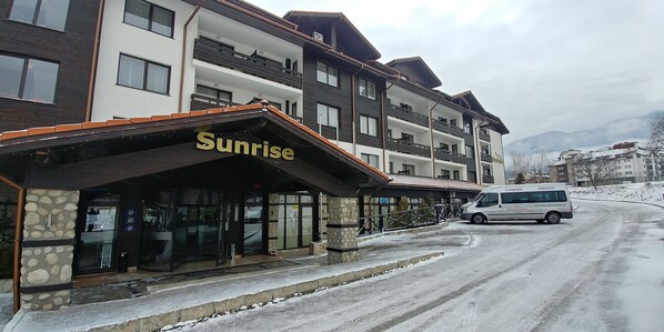 Et hotel i flere etager, der hedder 'Sunrise', med en stenfassade og en overdækket indgang.
