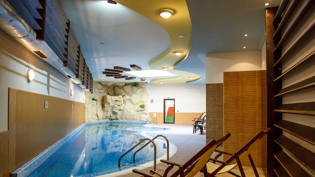 Una piscina interior con suelo de madera, pared de roca y zona de estar con sillas.