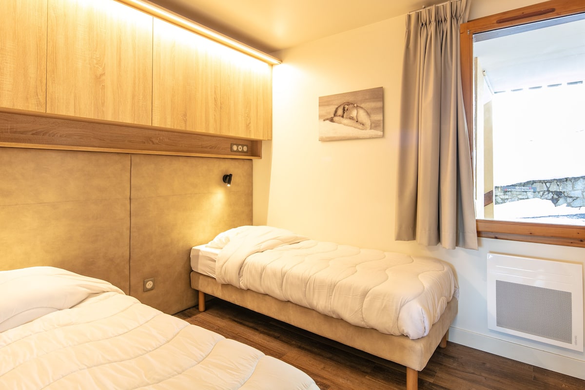 A bedroom with a bed, a headboard, a wall-mounted light, a window with curtains, and a wall-mounted air conditioner.