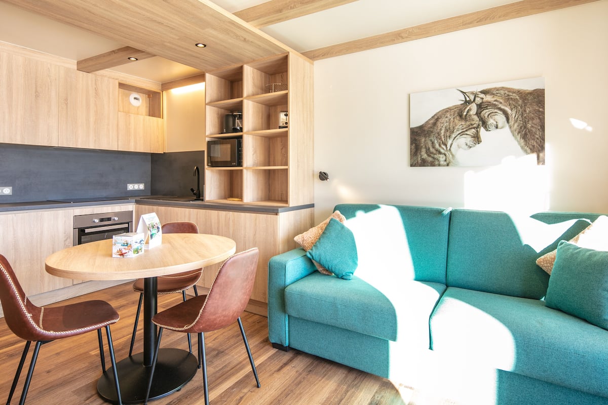 A modern kitchen with wooden cabinets, a built-in microwave, and a dining area with a round table and chairs.