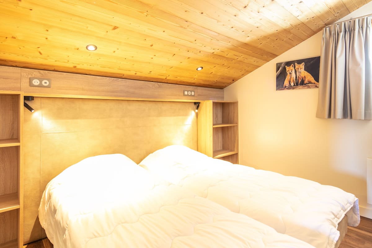 A bedroom with a wooden headboard, a bed with white bedding, a painting of foxes on the wall, and a window with curtains.