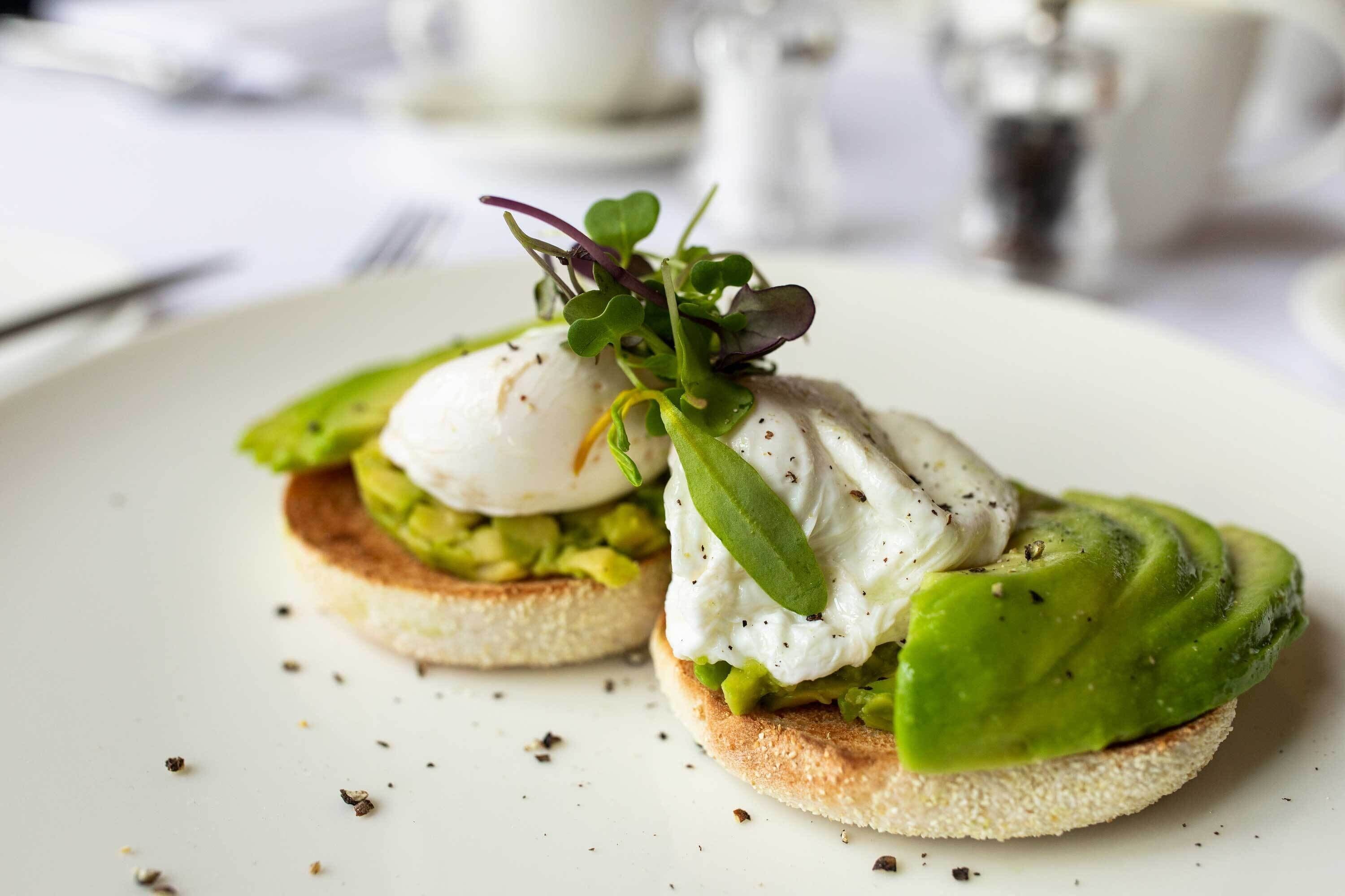 A breakfast dish with poached eggs, avocado, and greens on a slice of bread.