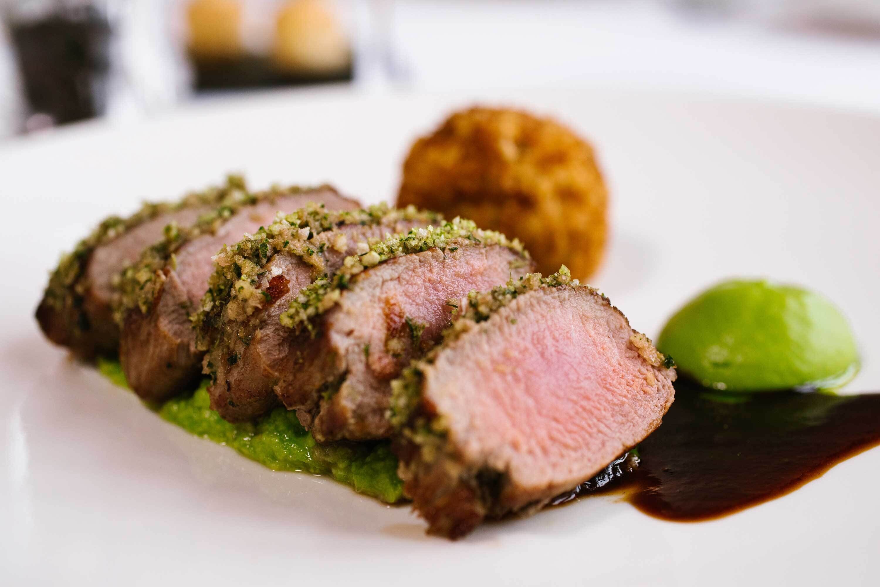 A dish of sliced meat with a green sauce and a dark sauce on a white plate.