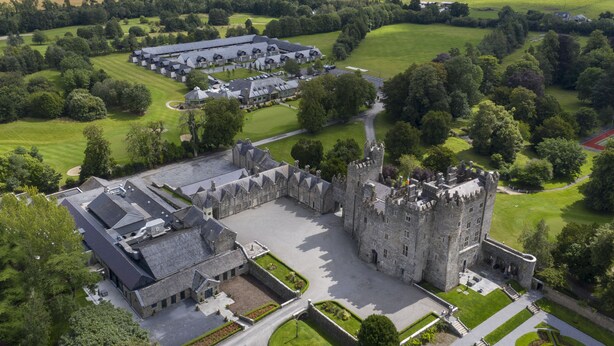 A castle with a large courtyard, surrounded by lush greenery and a modern building with a parking lot. - Kilkea Castle (Kilkea)