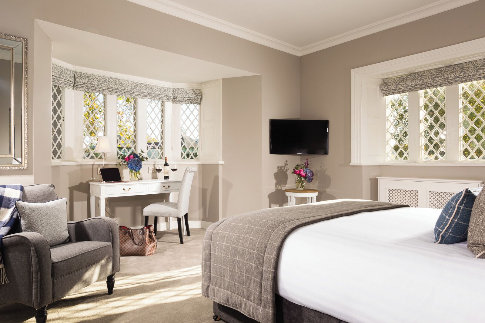 A bedroom with a bed, a desk, a chair, a TV, and a window with a lattice design.