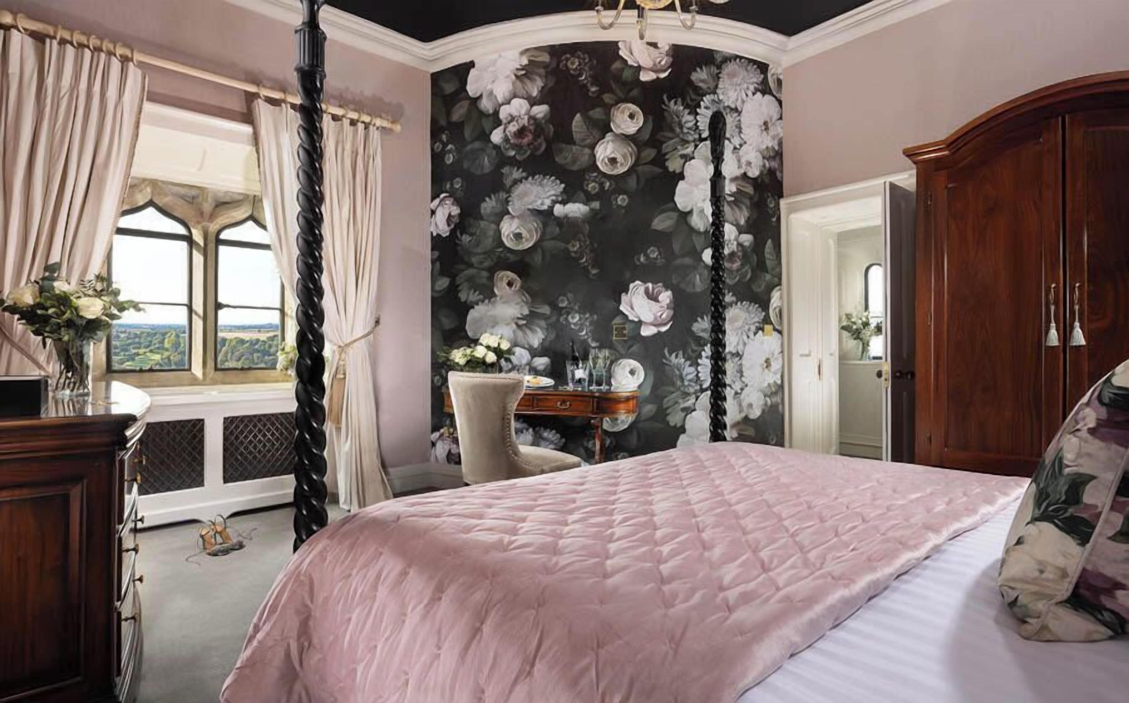 A bedroom with a large bed, a wooden wardrobe, a desk with a chair, and a window with curtains.