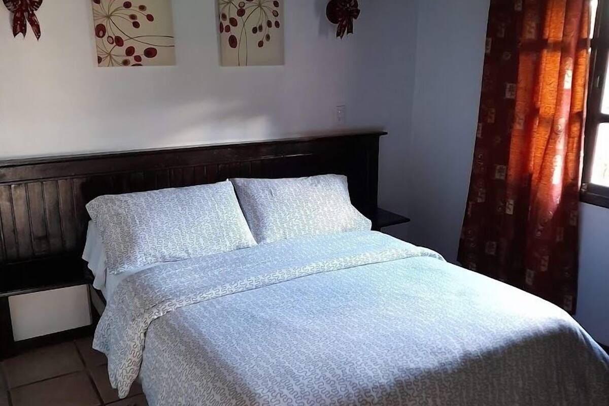 Une chambre à coucher comprenant un lit, deux lampes fixées au mur et trois œuvres d’art murales.