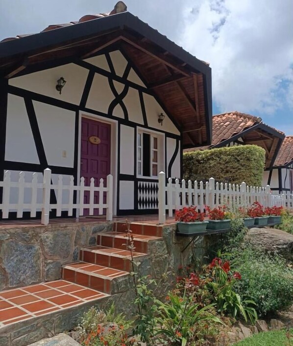 Una casa tradicional de entramado de madera con valla de piquetes blancos, escalones de piedra y una variedad de plantas en el jardín.