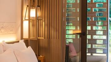 Habitación de hotel con cama, mesita de noche, lámpara y vistas a un espacio exterior con pared de ladrillo.