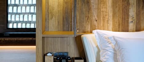 A hotel room with a wooden wall, a bed with white bedding, a bedside table with a telephone and a lamp, and a window with a view of a brick wall.