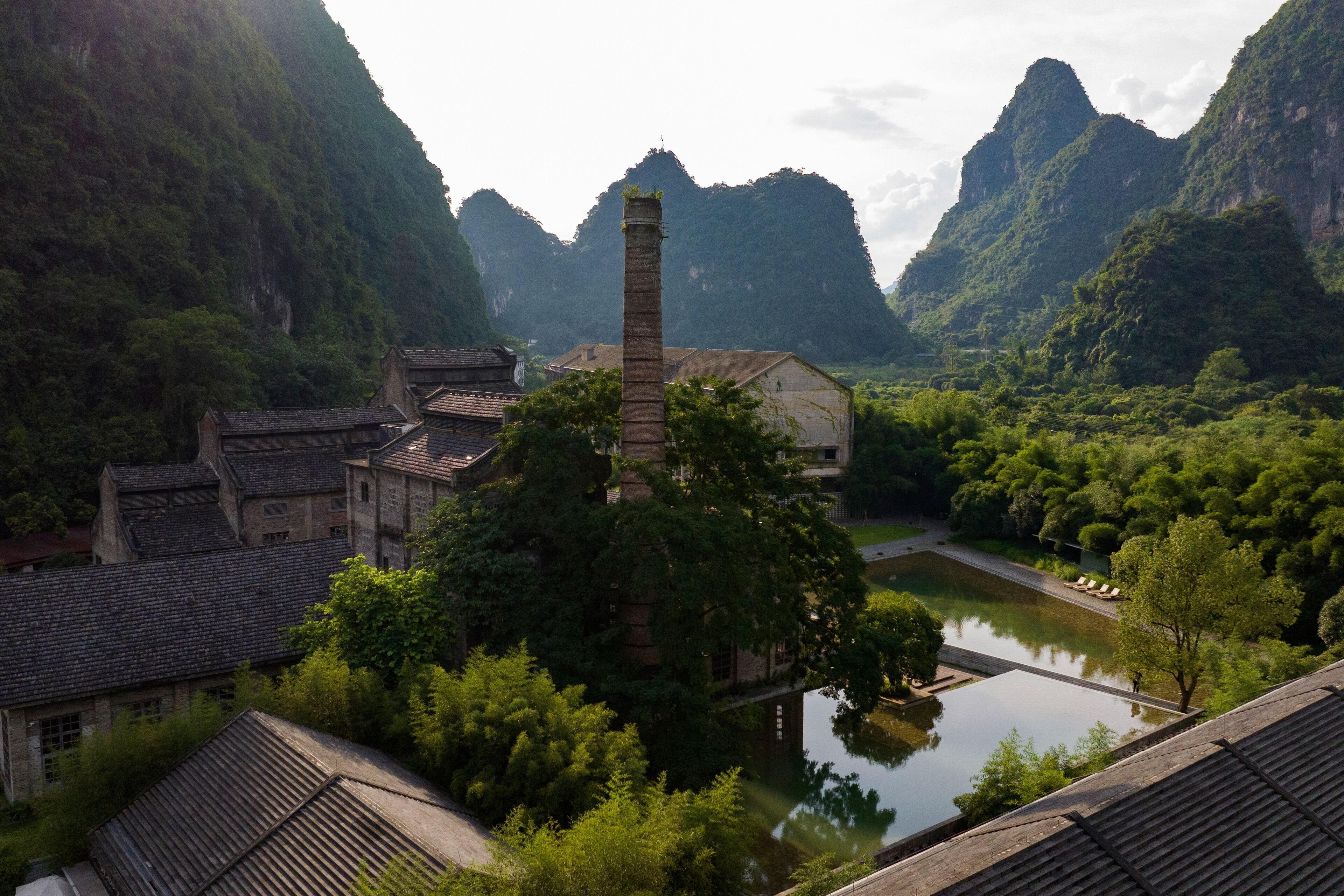 A traditional building with a prominent chimney, surrounded by lush greenery and a calm water body.
