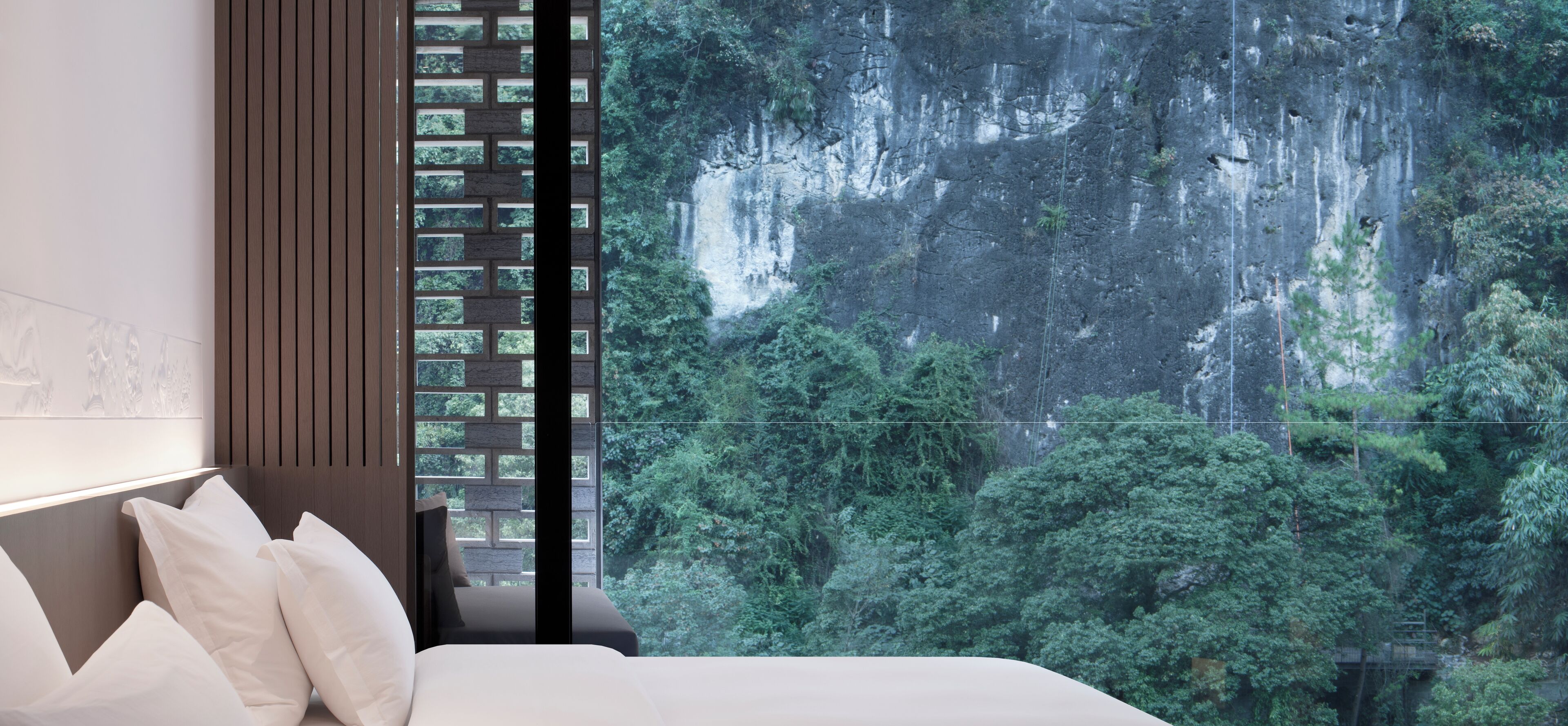A bedroom with a large window overlooking a forested cliff.