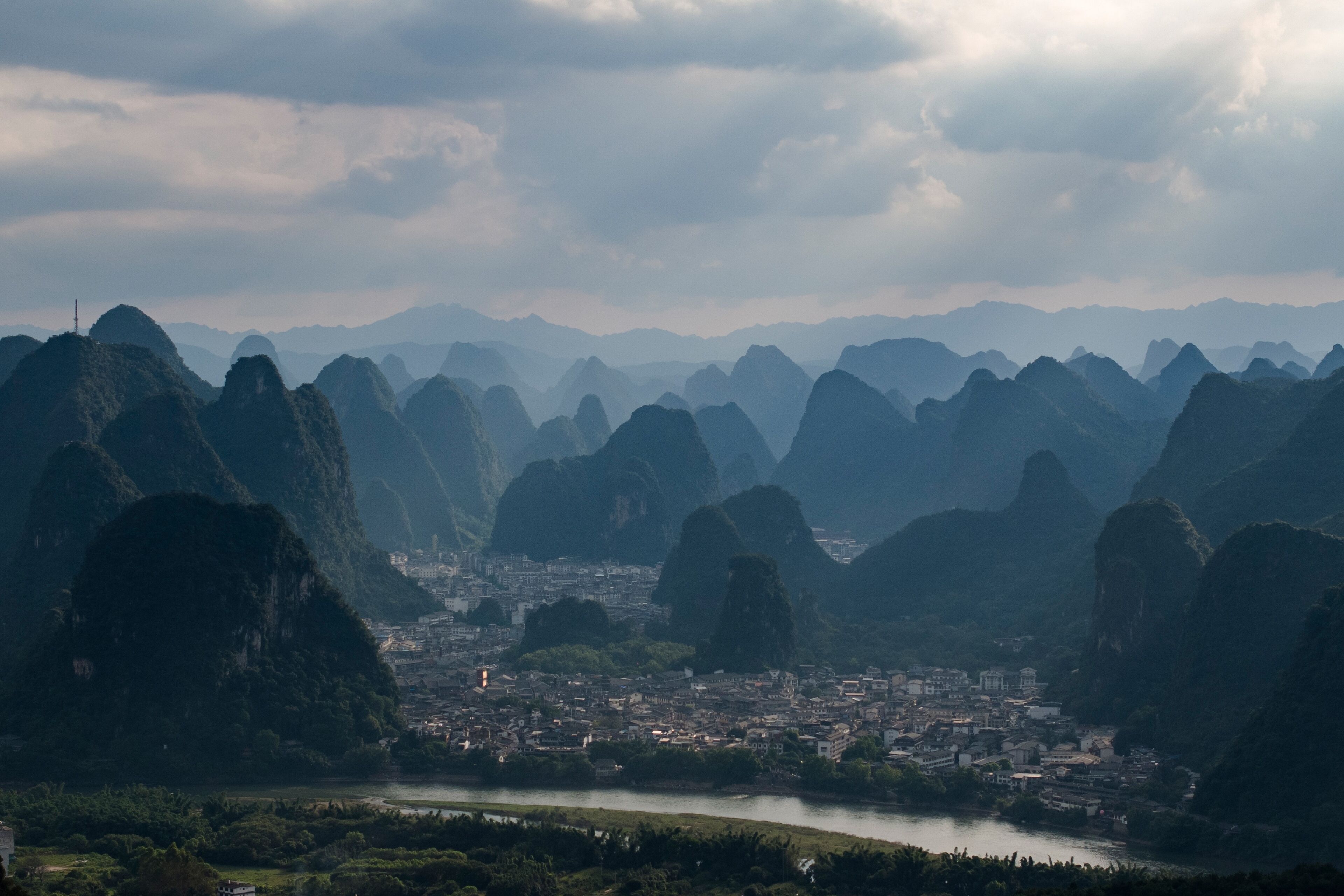 A panoramic view of a city nestled between limestone karsts, with a river flowing through the center.