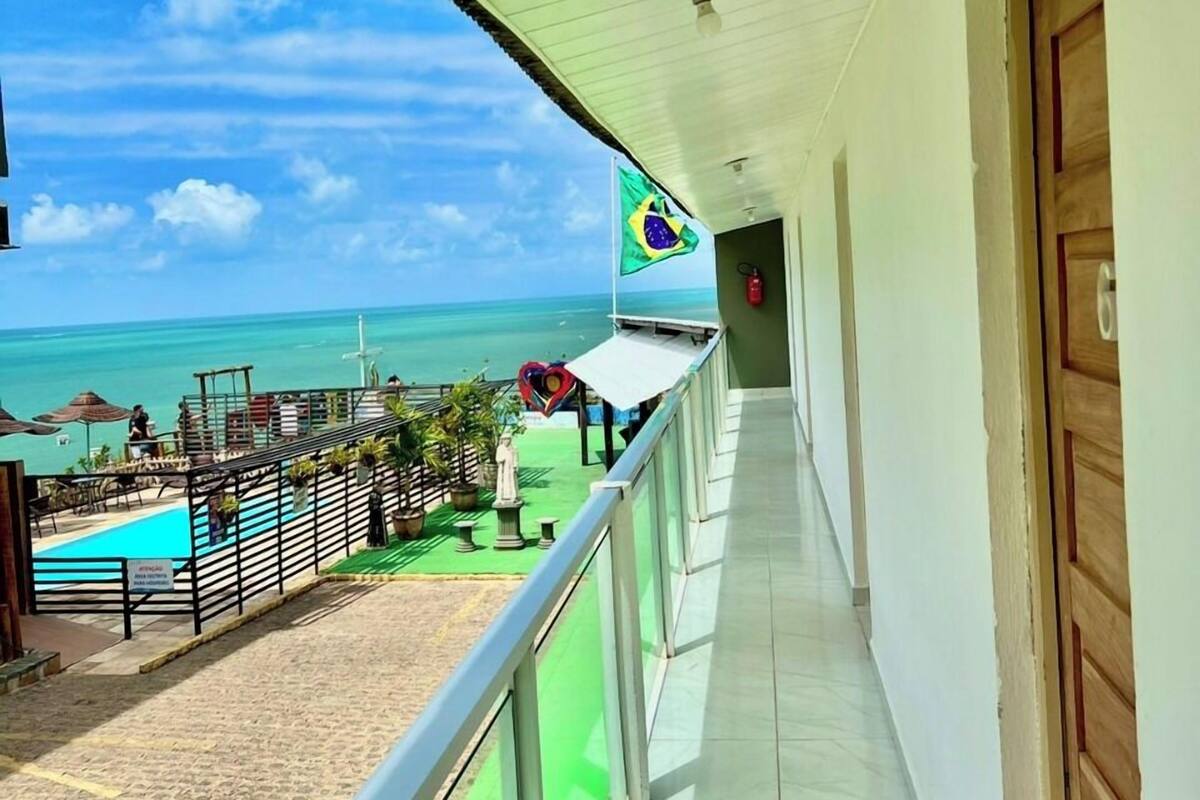A balcony with a view of a beach and ocean, a flag, and a pool area.