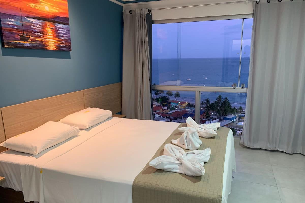 A hotel room with a bed, a view of the sea, and a painting on the wall.