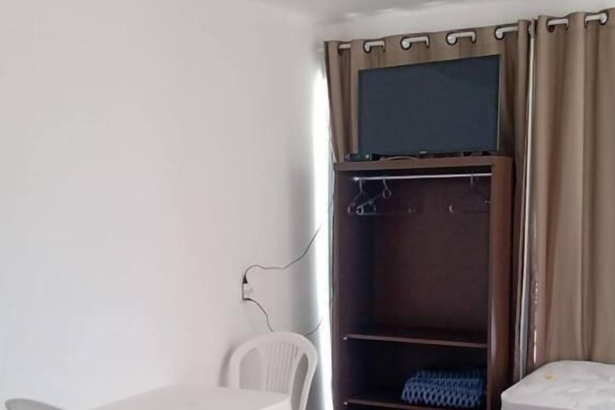 A room with a bed, a desk with chairs, a wardrobe, and a television.