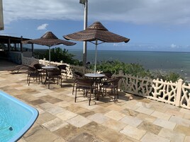 Zona de piscina con sillones y sombrillas con vista al mar.