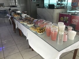 Una mesa de buffet con diversos alimentos y bebidas, un refrigerador Kibon y vista al mar a través de la ventana.