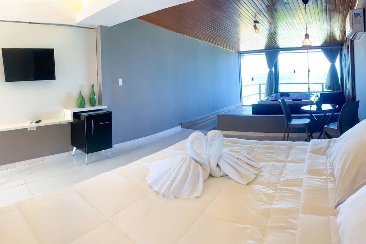 A modern hotel room with a large bed, a flat-screen TV, a small desk, and a seating area with a view.