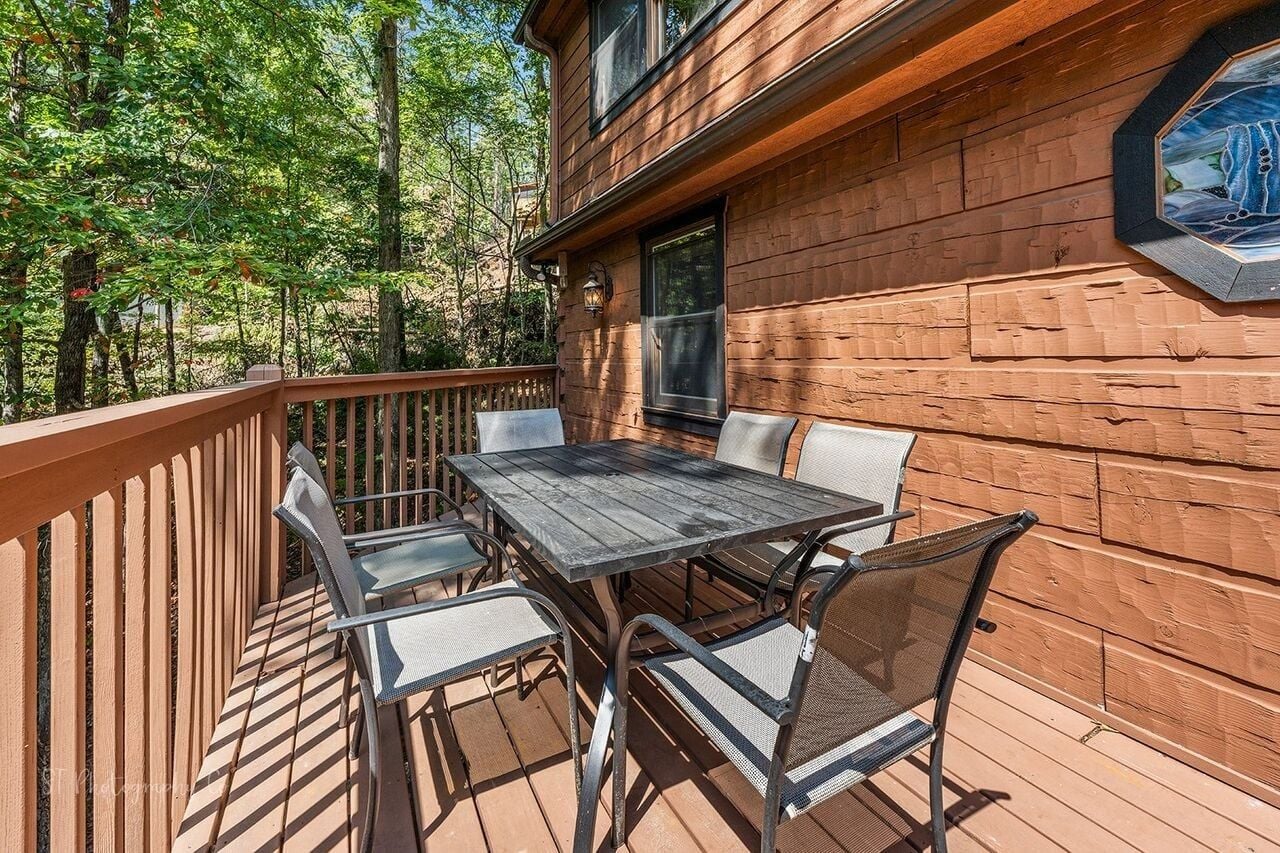 A wooden deck with a table and chairs, surrounded by a wooden fence, and a window with a view of trees.