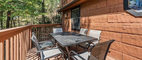 A wooden deck with a table and chairs, surrounded by a wooden fence, and a window with a view of trees.