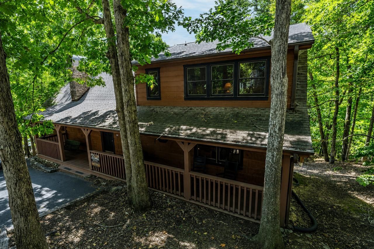 A cabin with a wooden exterior, a porch, and a view of the surrounding forest.