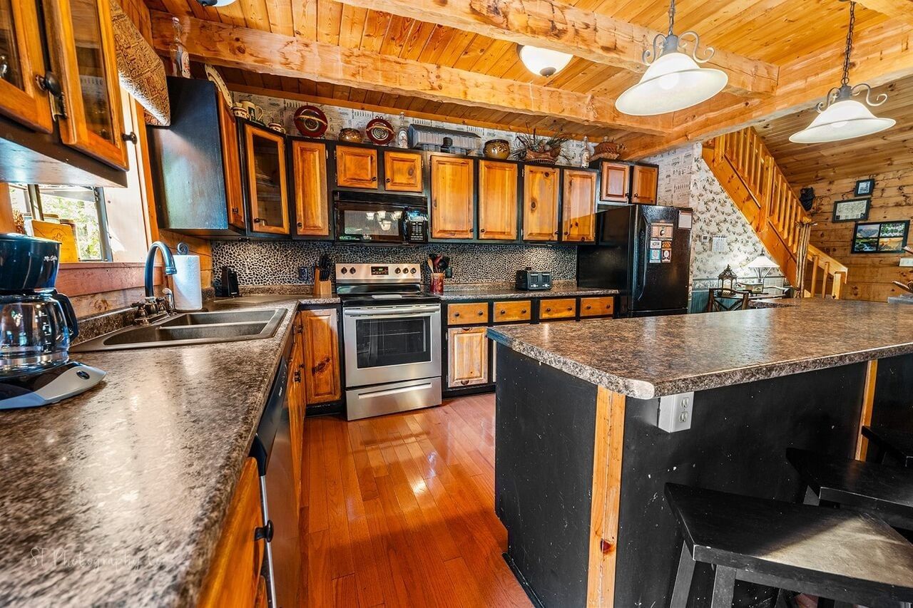 Una cocina con armarios de madera, encimera de granito, electrodomésticos de acero inoxidable y una escalera de madera.