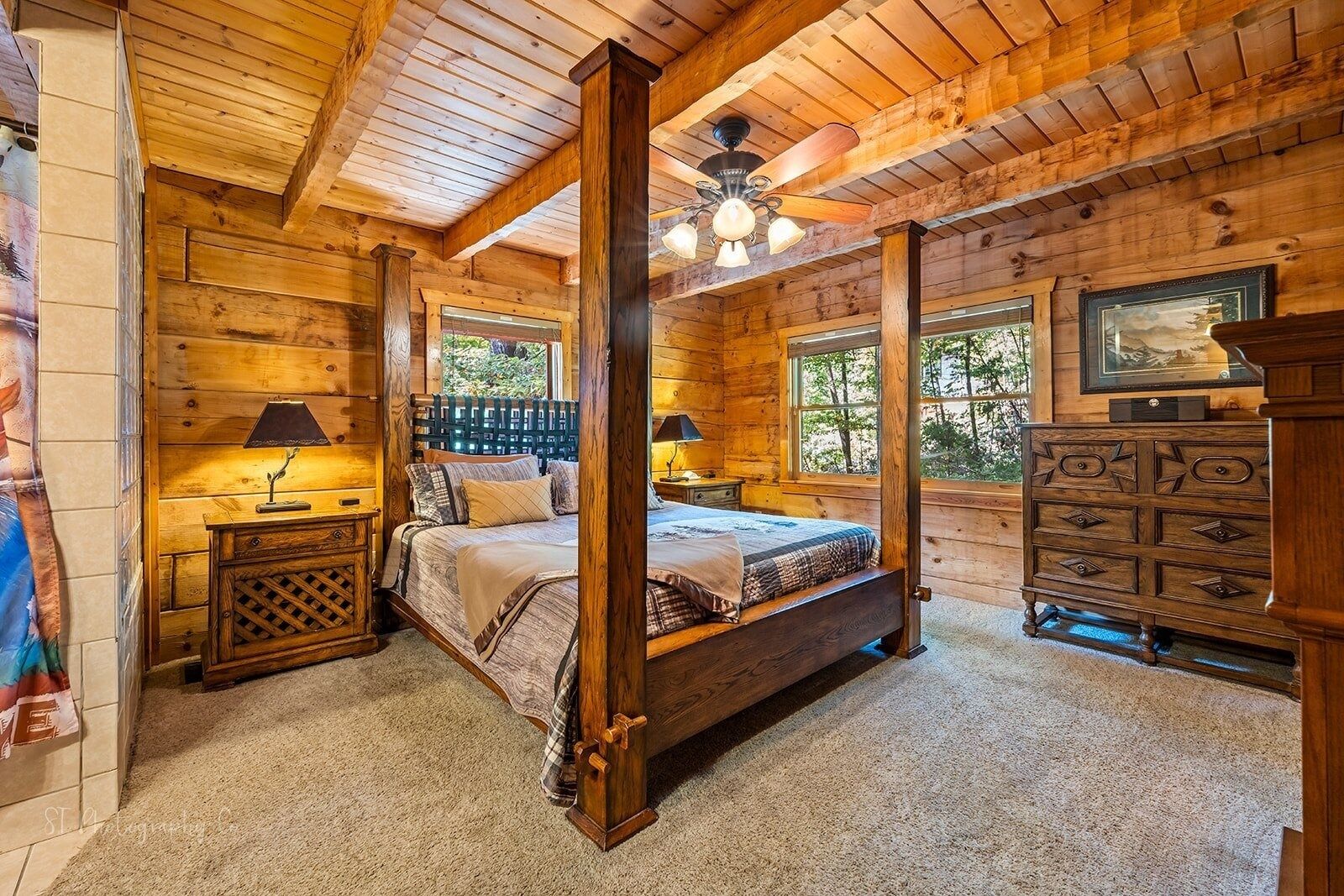 A log cabin bedroom with a four-poster bed, wooden dresser, and a ceiling fan.