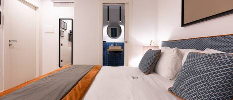 A modern hotel room with a neatly made bed, a bathroom with blue tiles, and a framed picture on the wall.