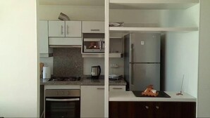 A modern kitchen with white cabinets, a stainless steel refrigerator, a stove, and a microwave. - Depto Costa Mansa (Coquimbo)