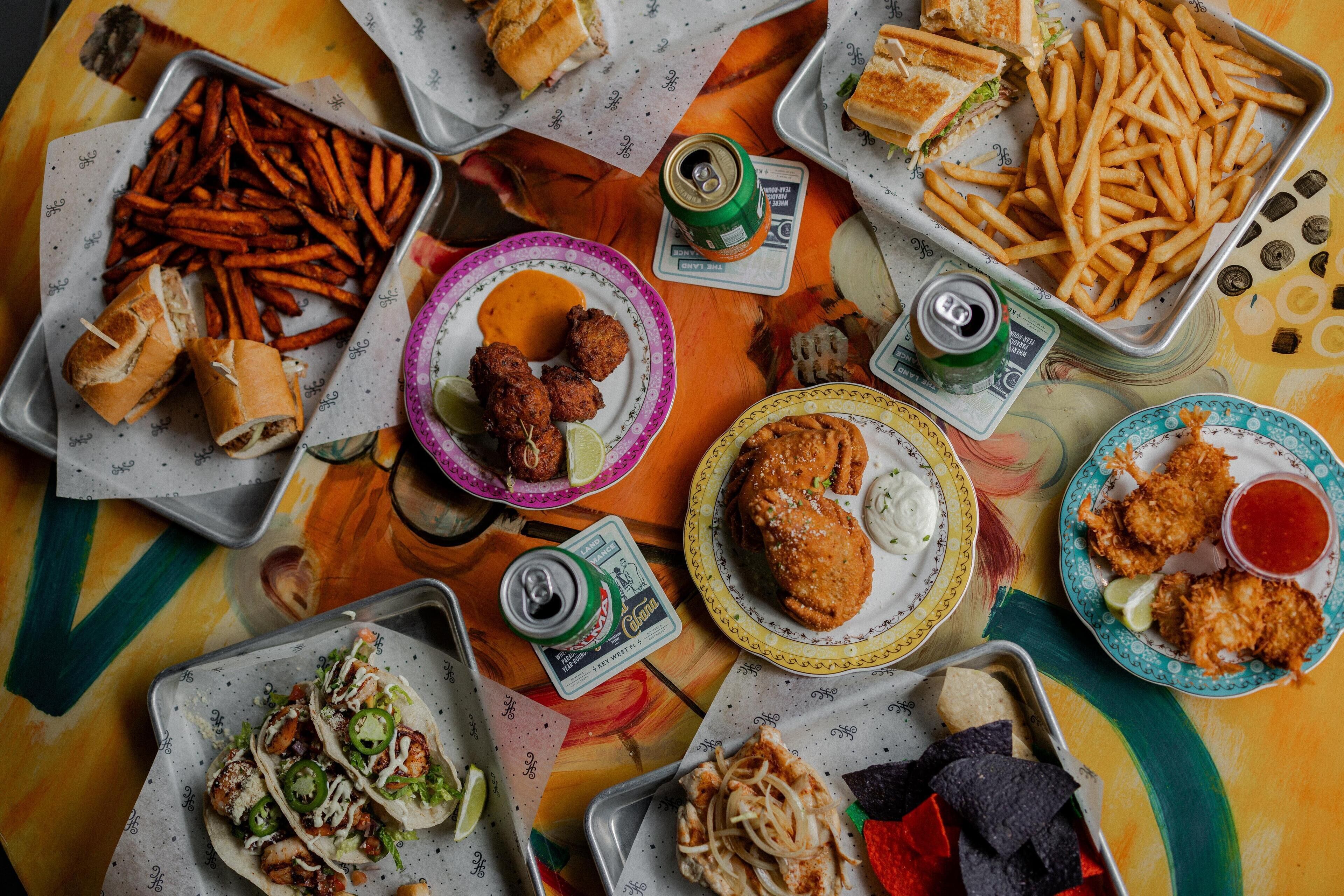 Une variété d’aliments, notamment des sandwichs, des frites et des tacos, sont disposés sur une table.